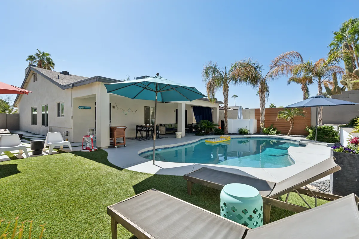 This image displays an inviting swimming pool surrounded by an outdoor seating area, palm trees, and umbrellas. The setting exudes a tranquil atmosphere ideal for lounging, swimming, or enjoying outdoor dining. The design suggests privacy and comfort, perfect for couples or small groups seeking relaxation.