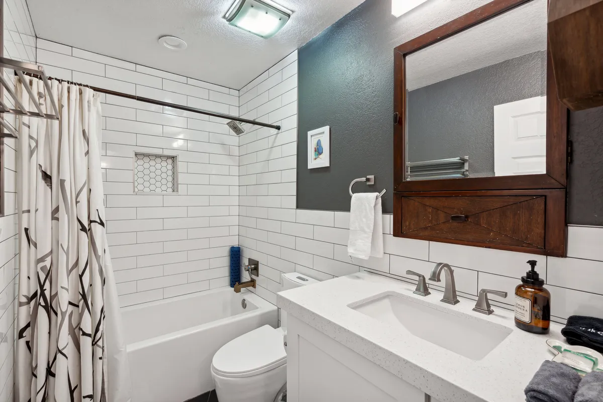 A bright, inviting second bathroom with a white bathtub, sink, mirror, and shower curtain. The room feels fresh, clean, and practical—ideal for families or guests.
