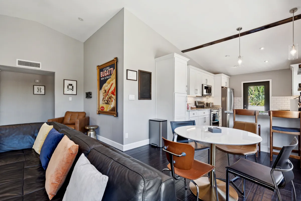An inviting interior featuring a comfortable leather sofa, a round dining table set for meals, and a view into the contemporary kitchen area. Framed artwork and tasteful décor add warmth and style, while the open-plan layout emphasizes togetherness.